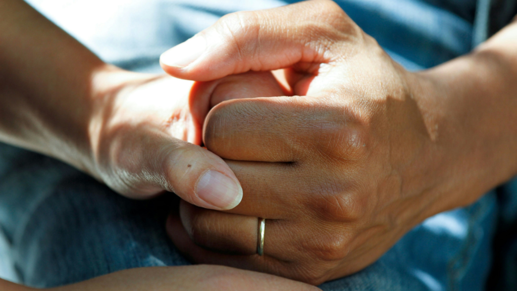 Two hands gently holding each other, symbolizing support, care, and compassion for those affected by lung cancer